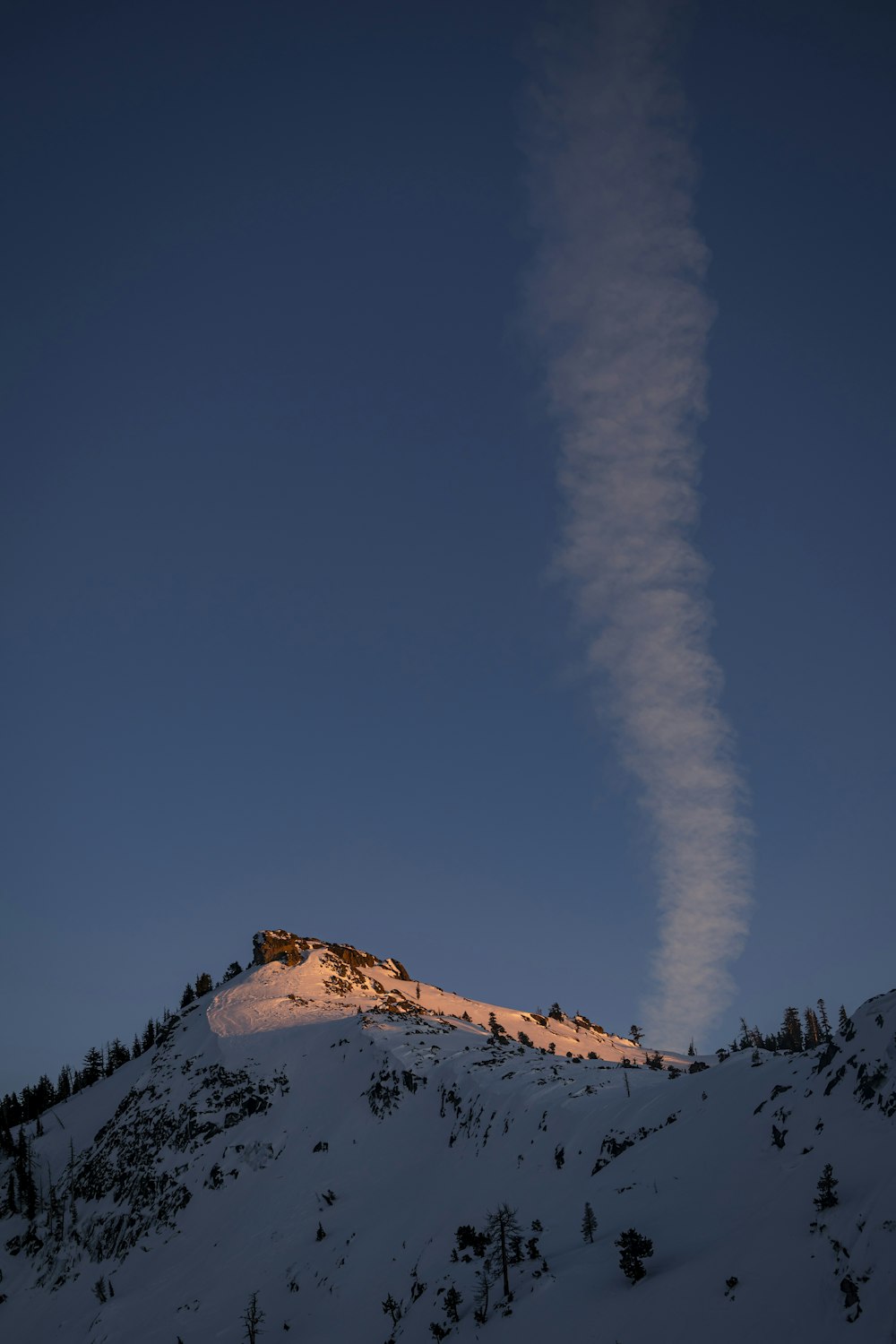 a long cloud of smoke rising from the top of a mountain