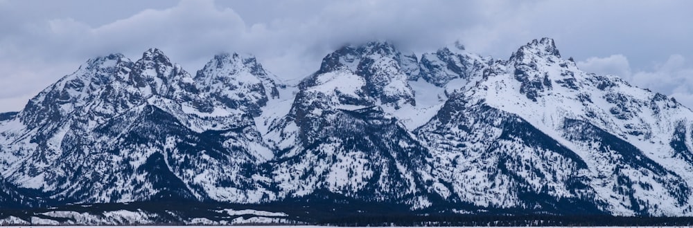 a mountain range covered in snow under a cloudy sky