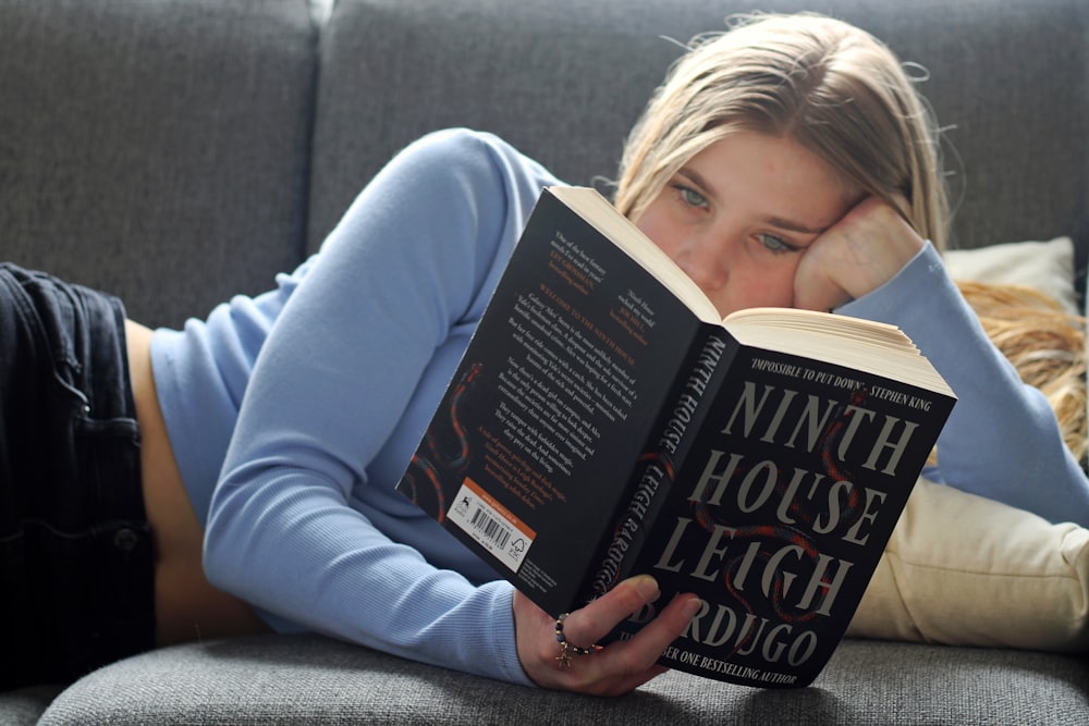 a woman laying on a couch reading a book