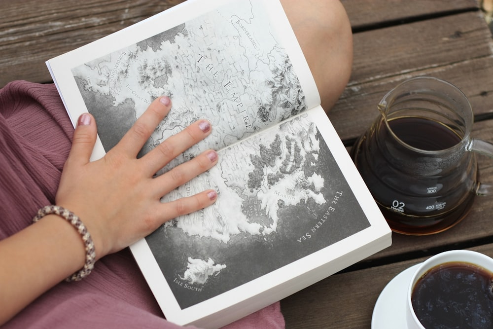 a person sitting on a bench with a book and a cup of coffee