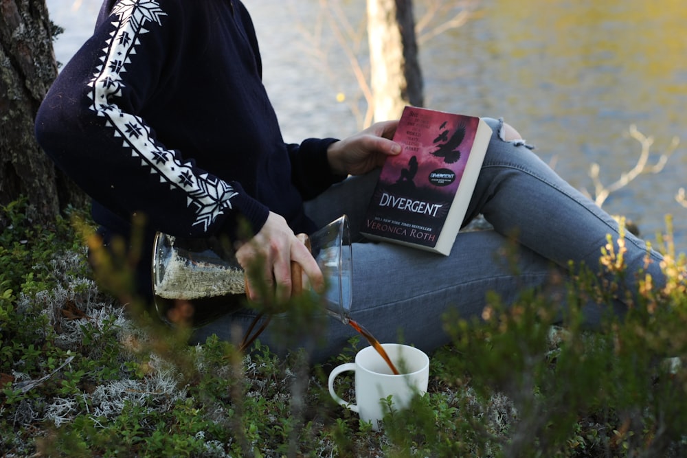 a woman sitting next to a tree holding a book