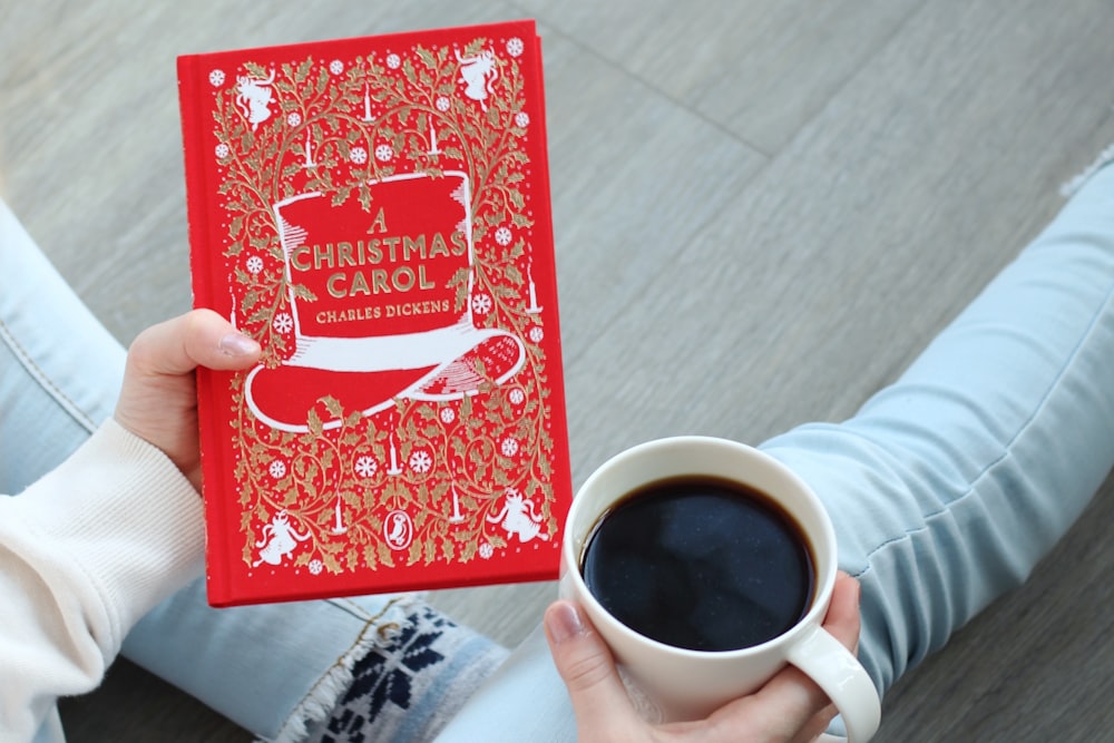 a person holding a red christmas card next to a cup of coffee