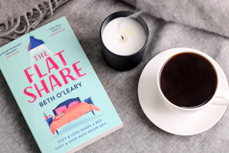 a cup of coffee next to a book and a candle