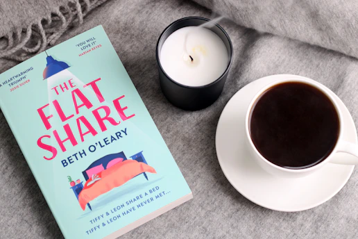 a cup of coffee next to a book and a candle