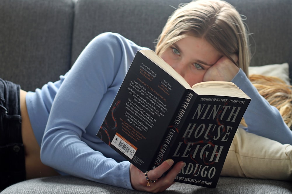 a woman laying on a couch reading a book