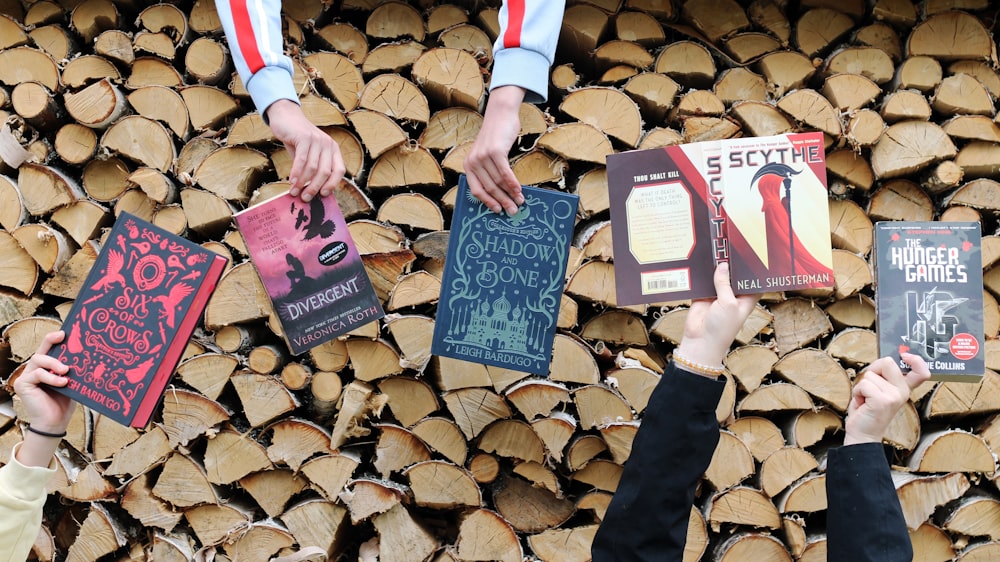 a group of people holding up books in front of a pile of logs