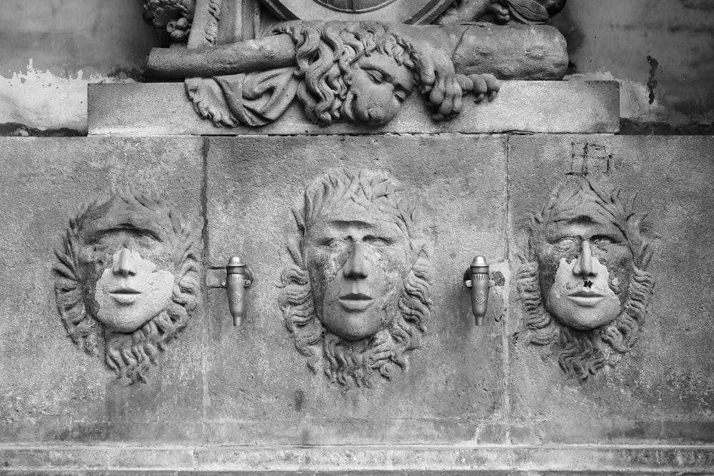 a black and white photo of three faces on a wall