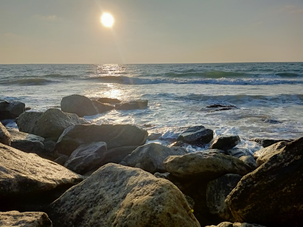 the sun is shining over the ocean and rocks