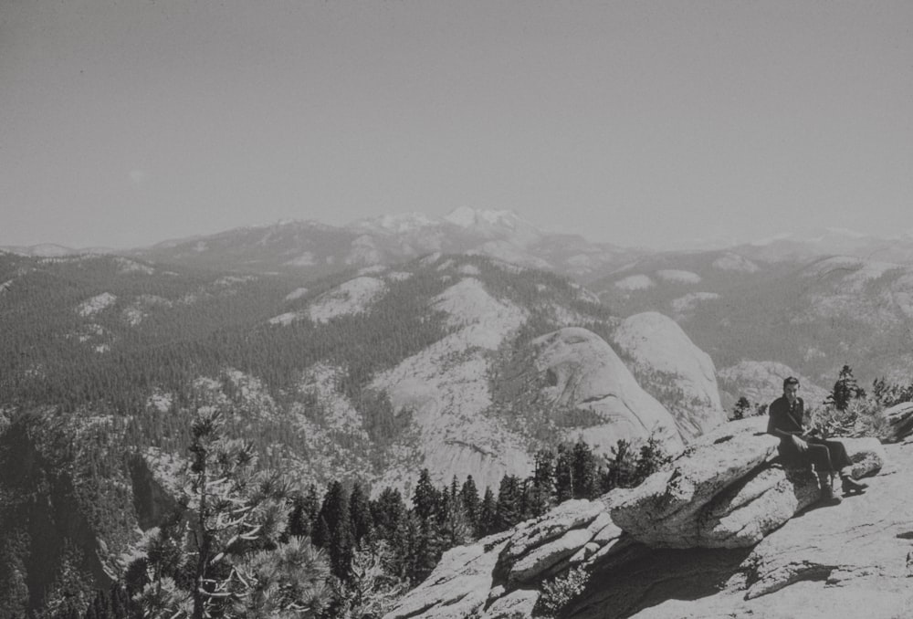 a black and white photo of a man sitting on top of a mountain