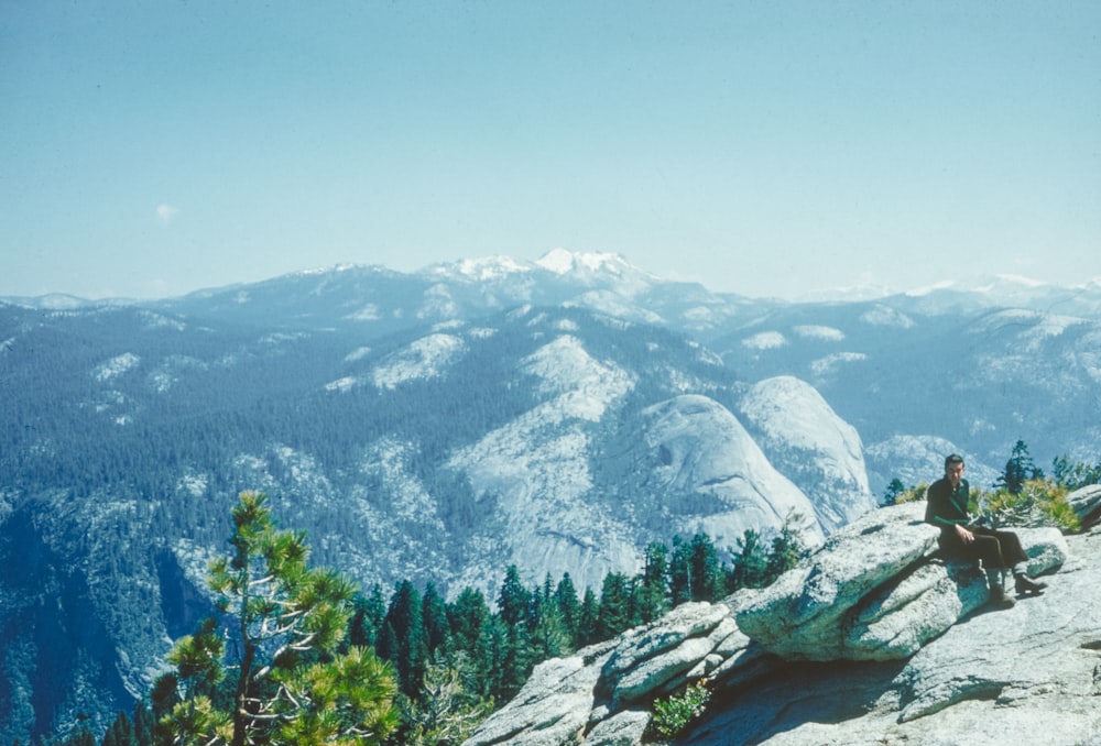 a man sitting on top of a mountain next to a forest