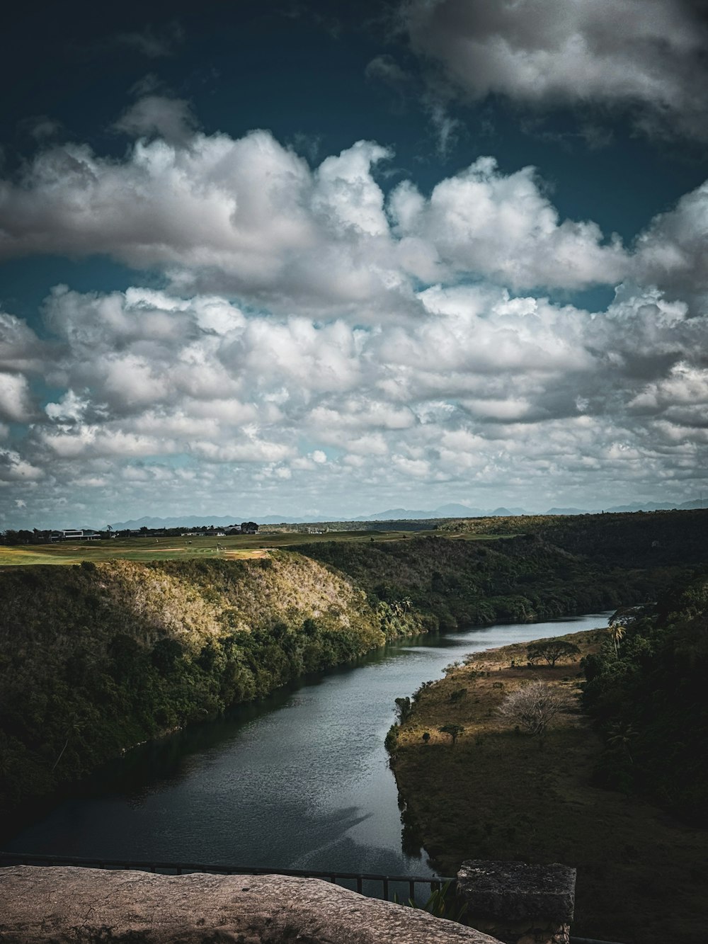 a river running through a lush green countryside under a cloudy sky