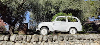 an old white car parked on a stone wall