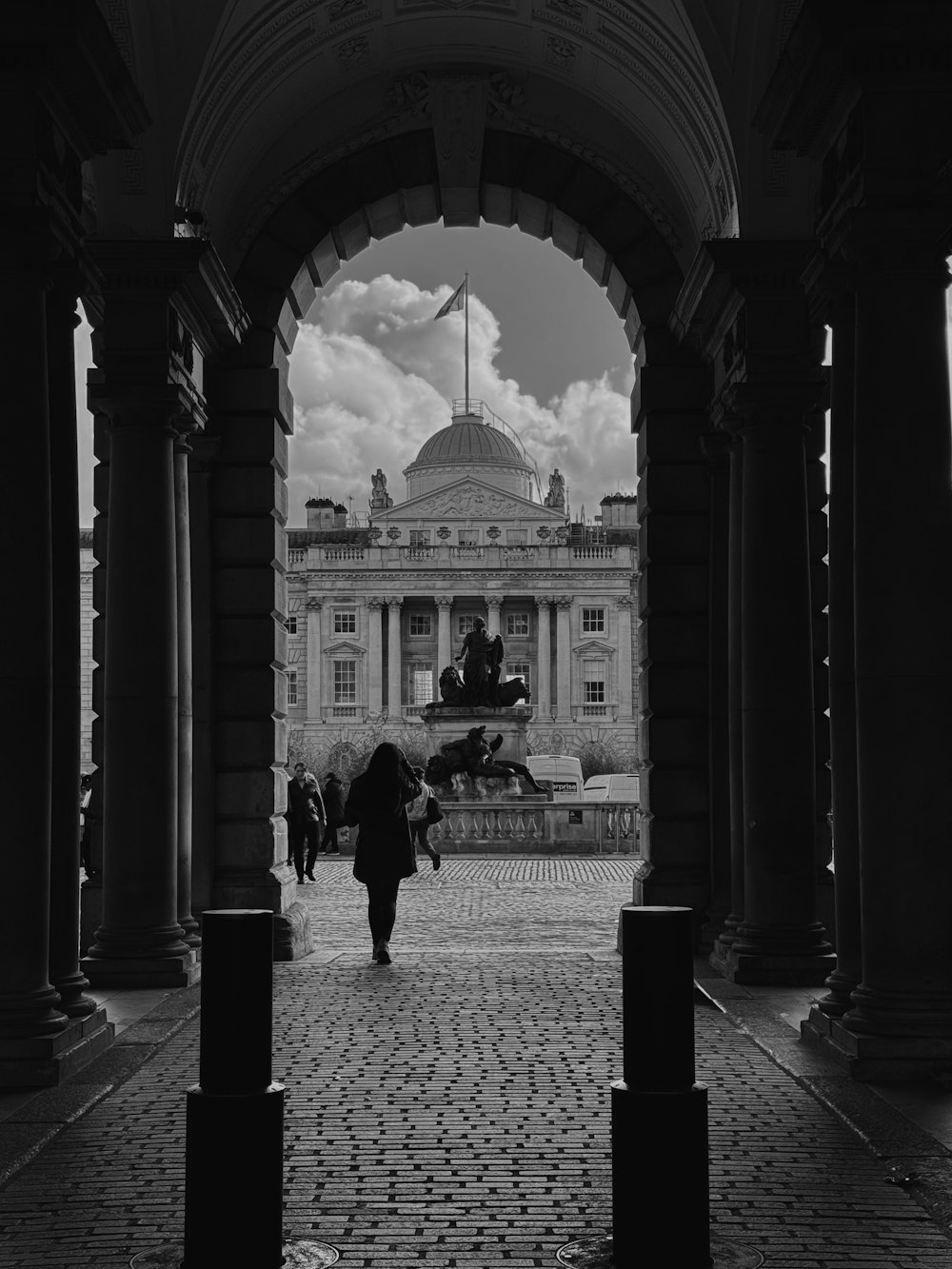 a black and white photo of a person walking through an archway