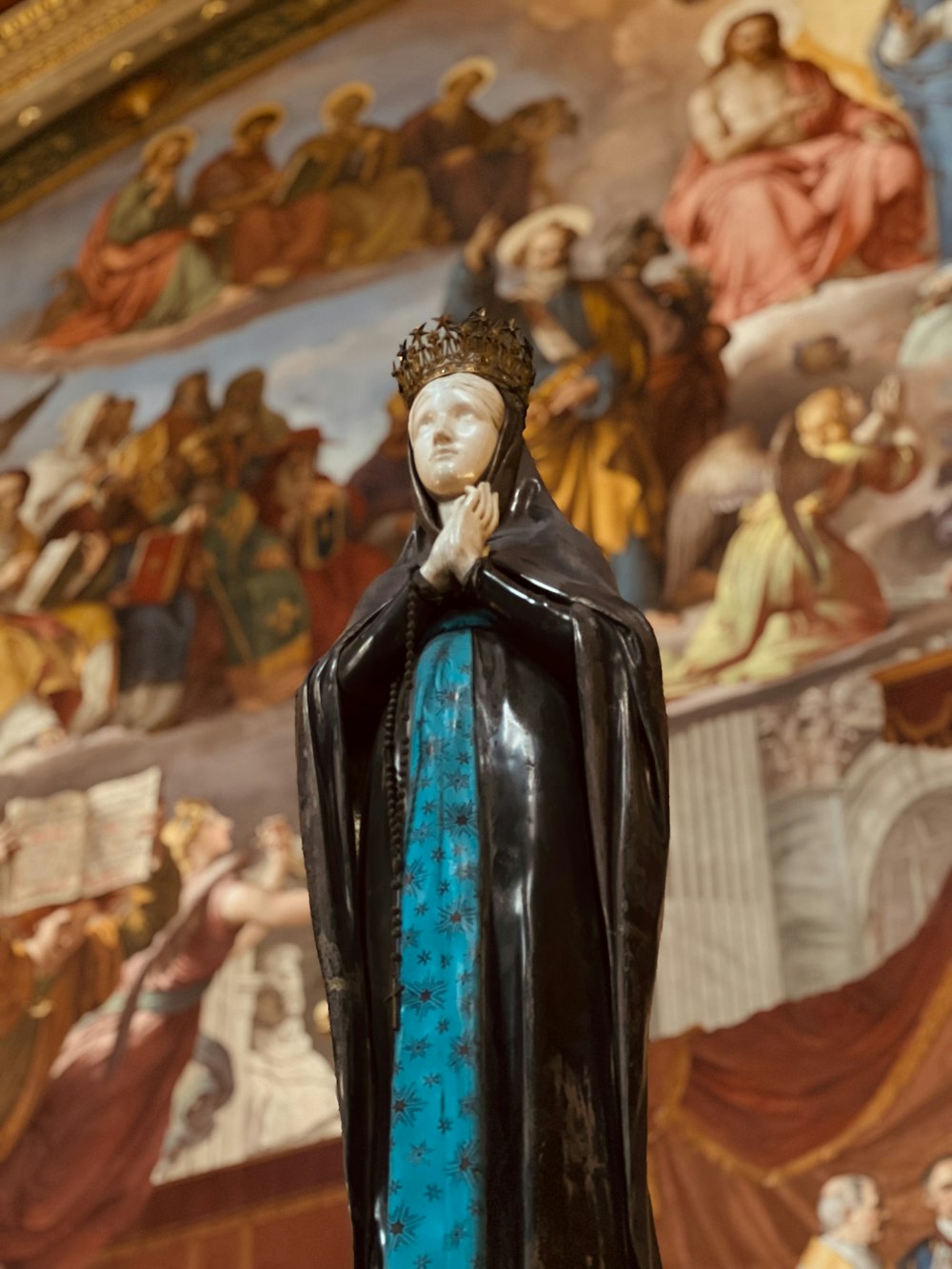 a statue of a woman with a blue dress in front of a painting