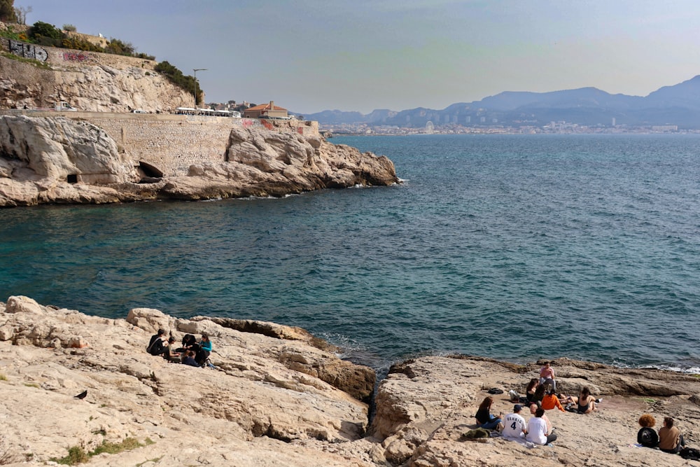 a group of people sitting on top of a rocky cliff next to the ocean