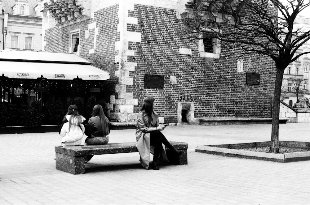 a couple of people sitting on a bench next to a tree