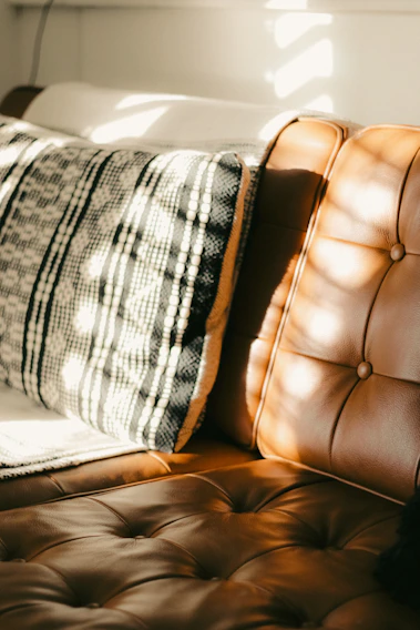 Plaid pillow beside a tufted leather couch in warm light