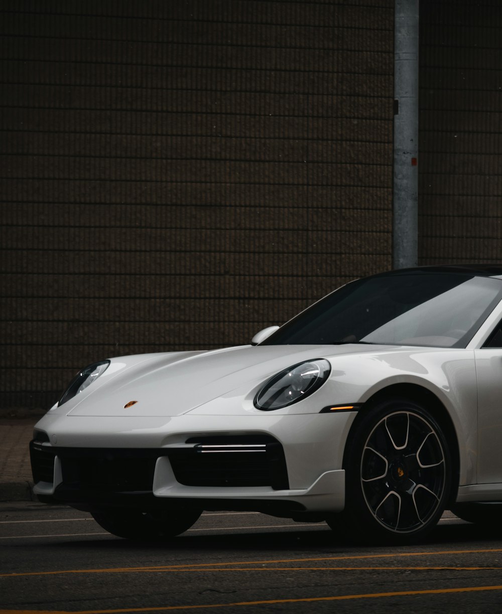 a white porsche sports car parked in front of a brick wall
