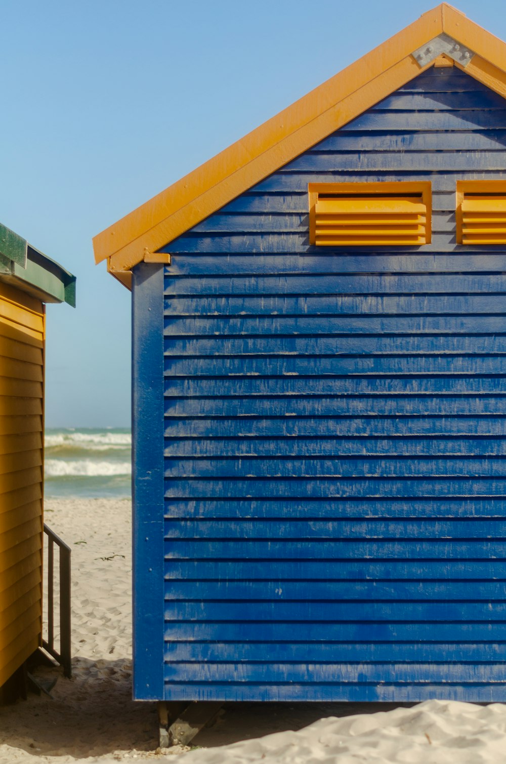 una cabaña de playa azul y amarilla sentada en la parte superior de una playa de arena