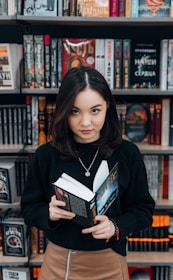 a woman standing in front of a bookshelf holding a book