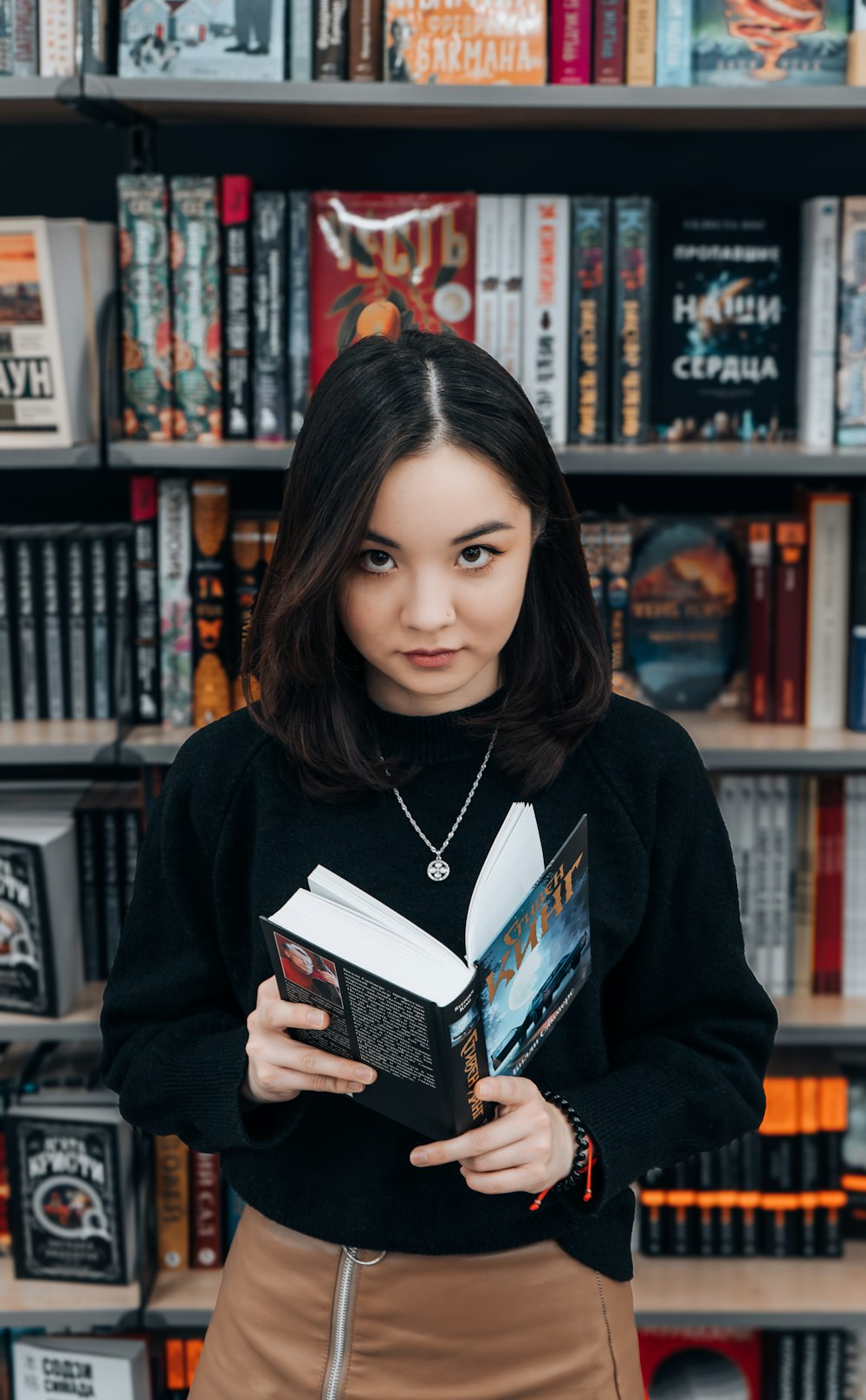 a woman standing in front of a bookshelf holding a book