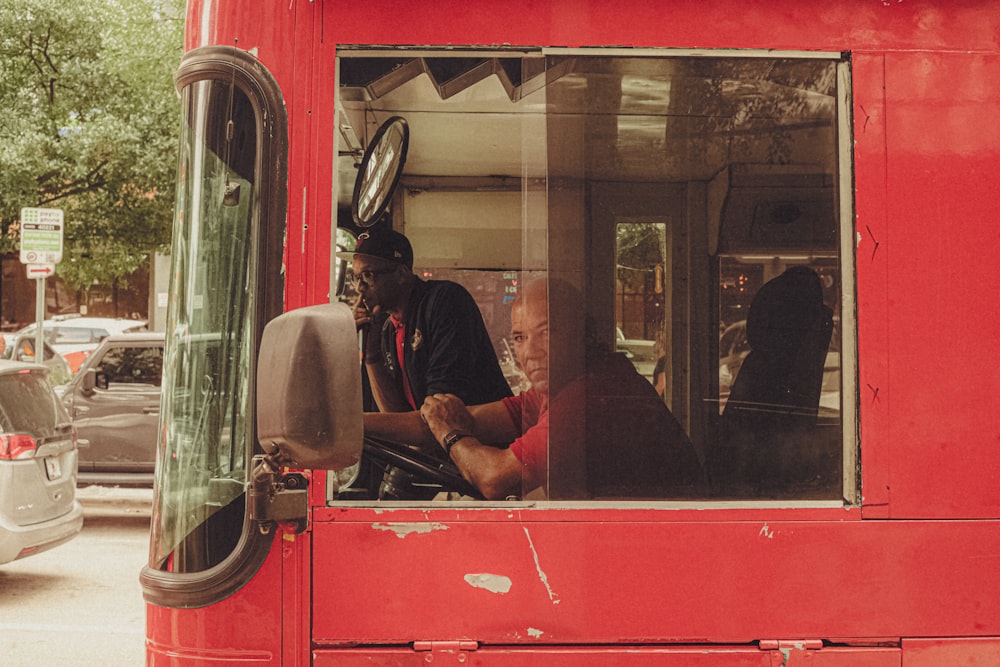 a man sitting in the driver's seat of a red bus