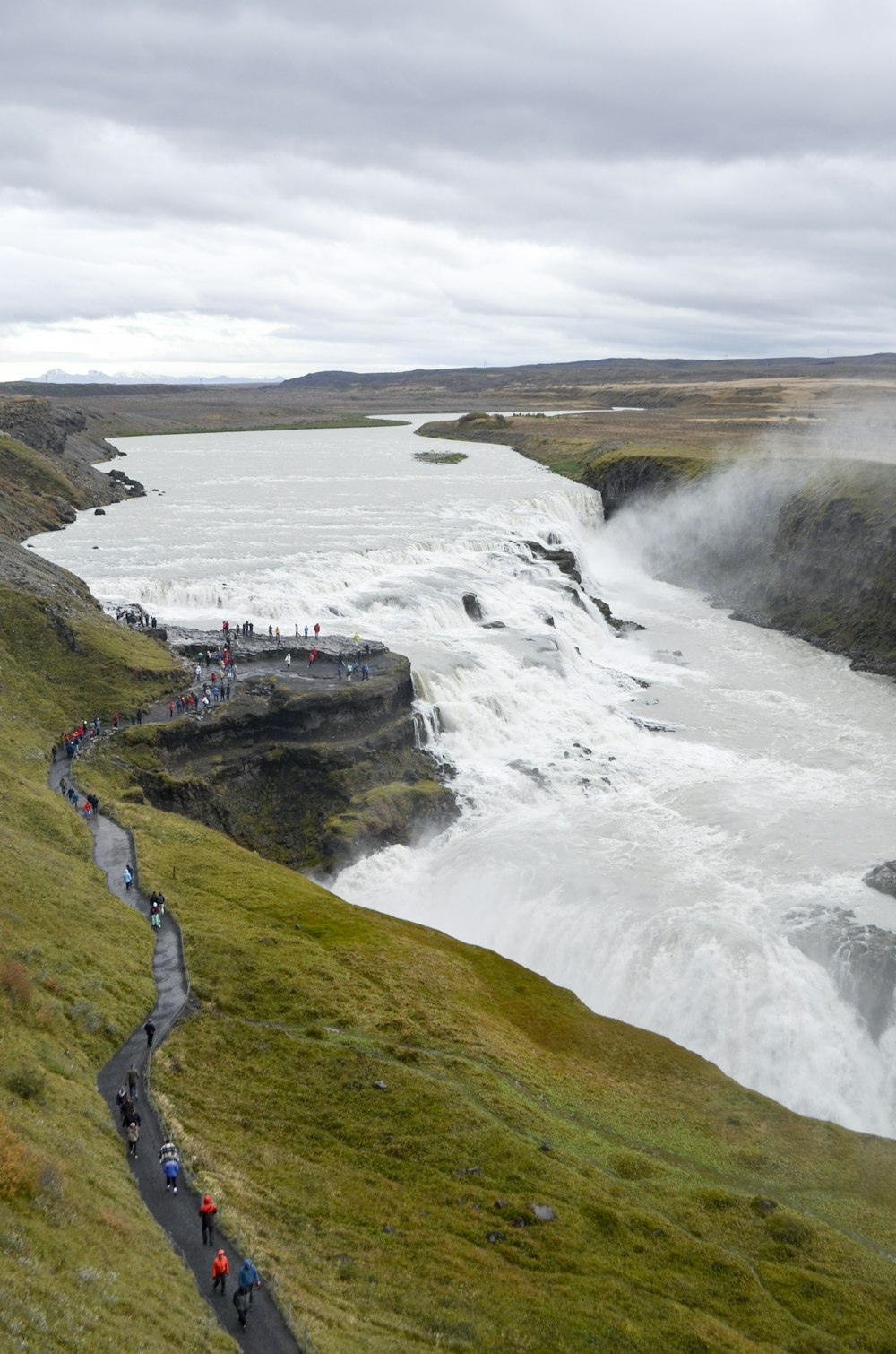 a group of people walking up a hill next to a river