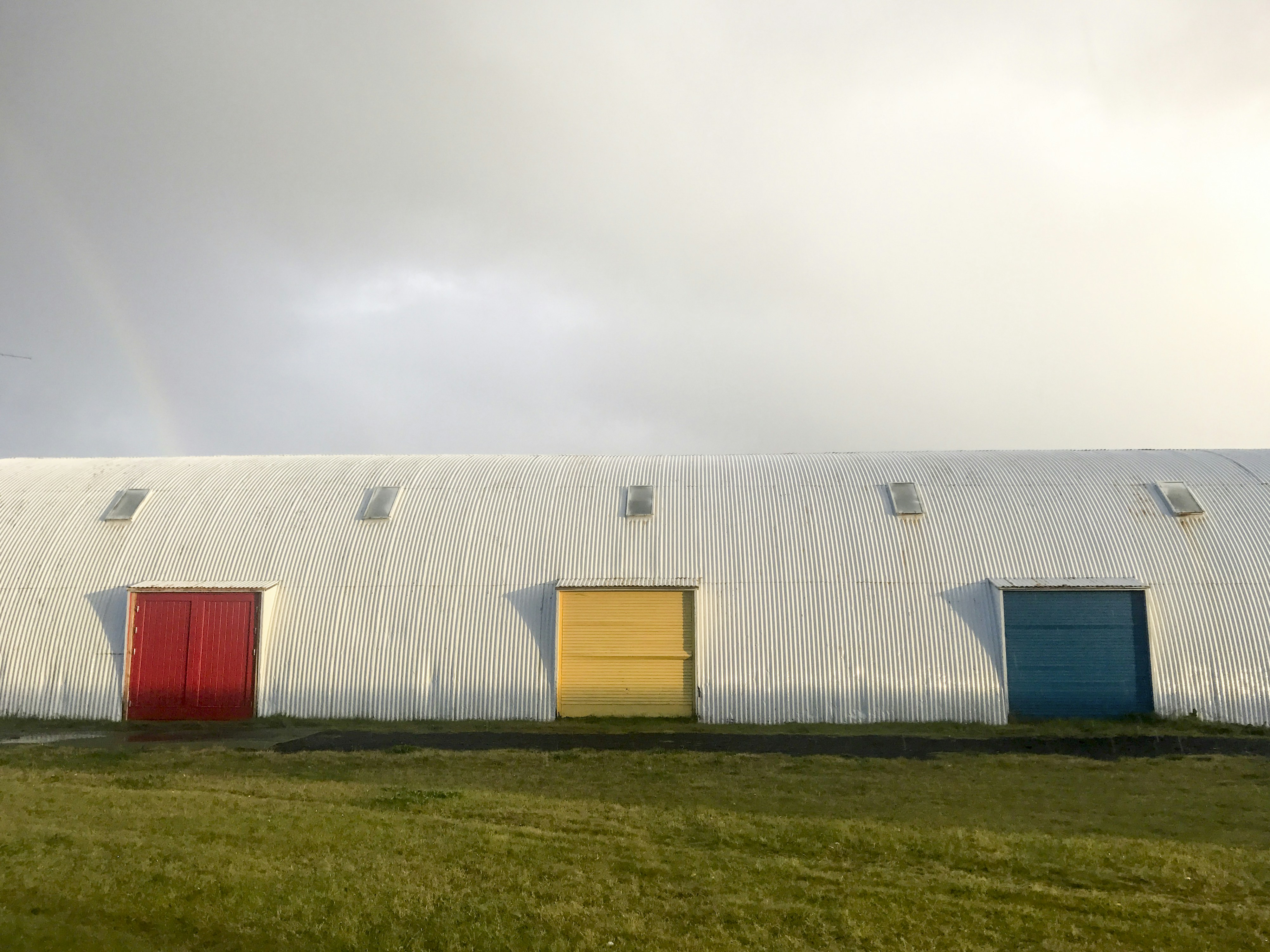 a white building with three doors and a rainbow in the background