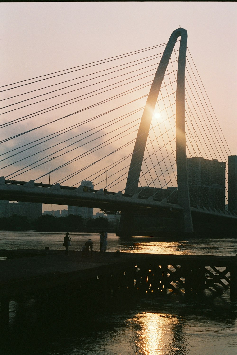 the sun is setting over a bridge over a body of water