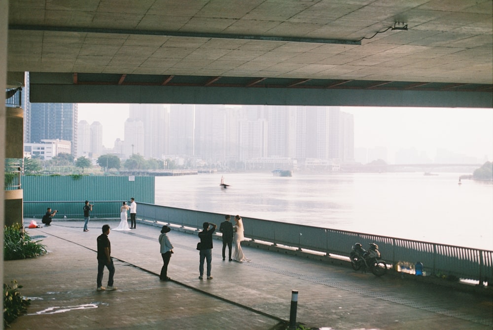 a group of people standing under a bridge next to a body of water