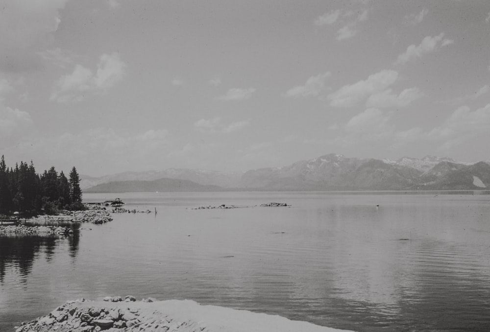 a black and white photo of a lake with mountains in the background