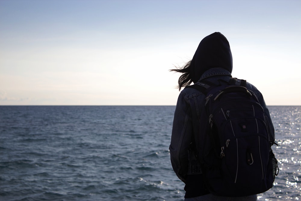 eine Person mit einem Rucksack, die auf das Meer blickt