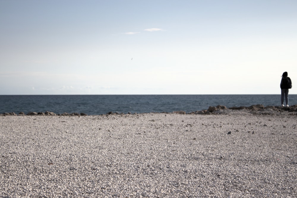 eine Person, die an einem Strand steht und auf das Meer blickt
