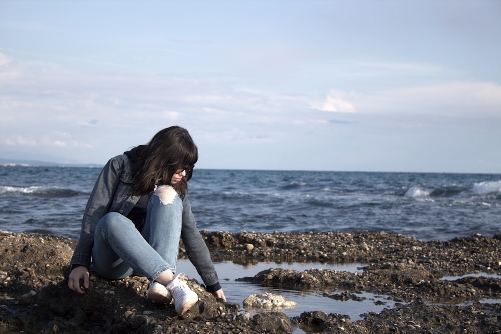 a woman sitting on a rocky beach next to the ocean
