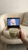 a person holding a cup of green tea in front of a laptop