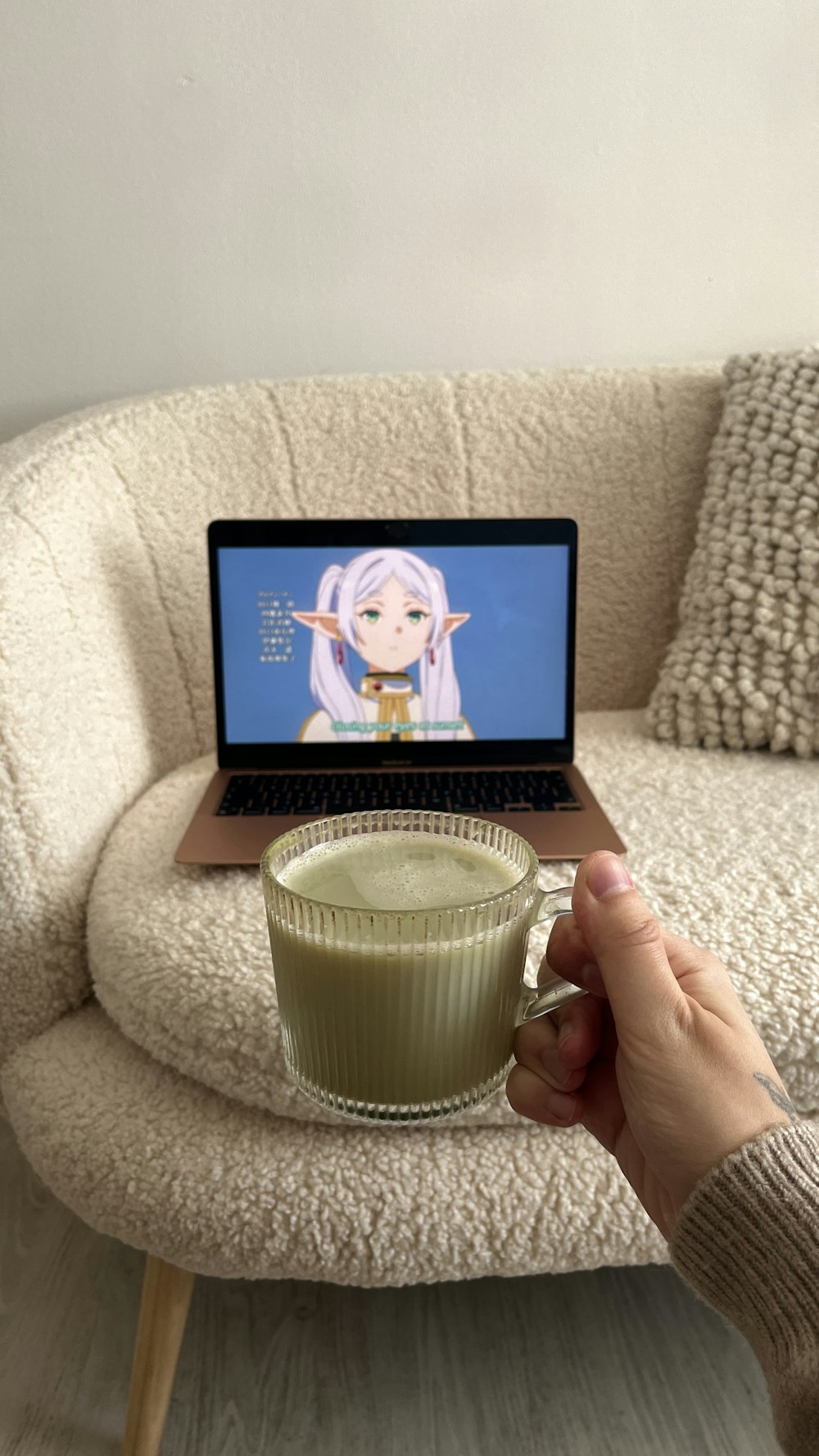 a person holding a cup of green tea in front of a laptop