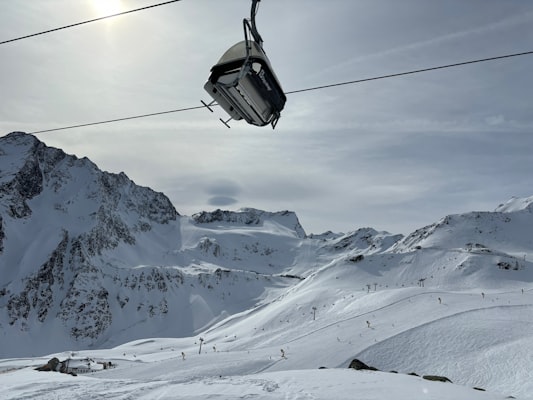 A gondola cabin riding its cable high above wide glacier pistes dotted with skiers