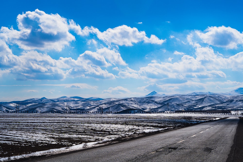 uma longa estrada com neve no chão e montanhas ao fundo