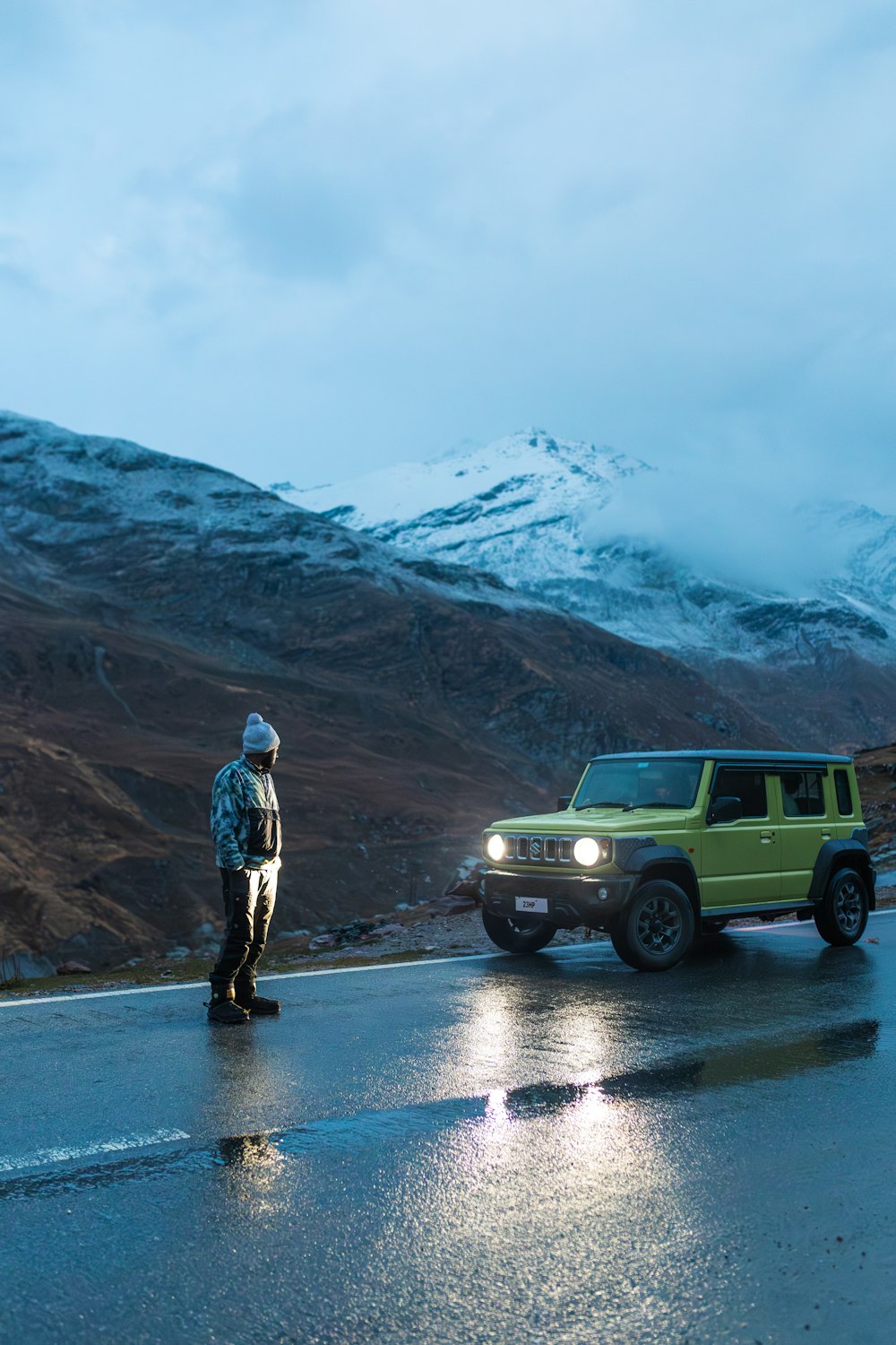 a man standing on the side of a road next to a green jeep