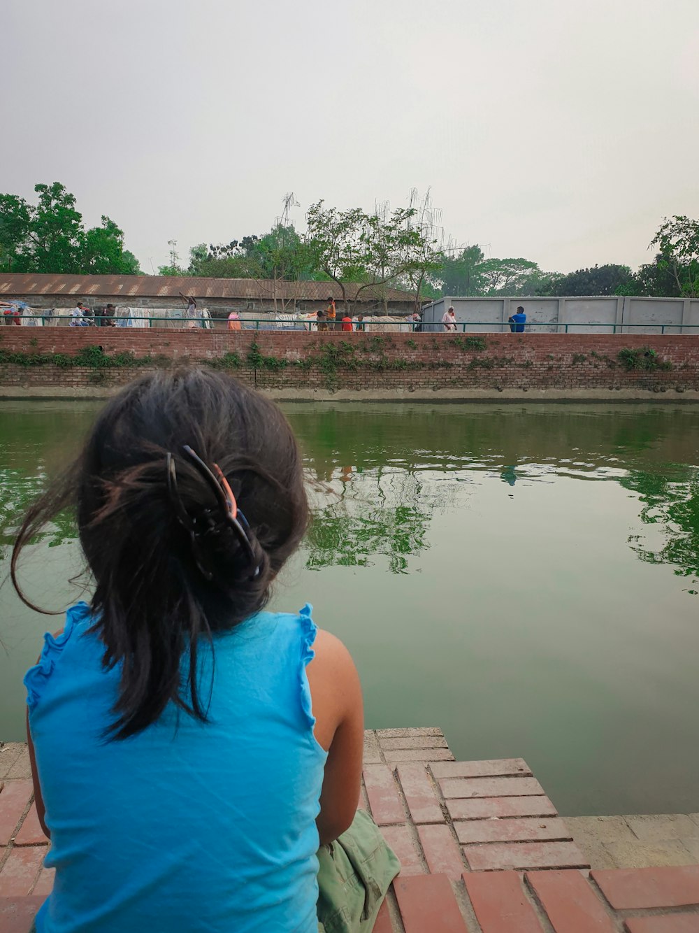 a little girl sitting on a dock looking at the water