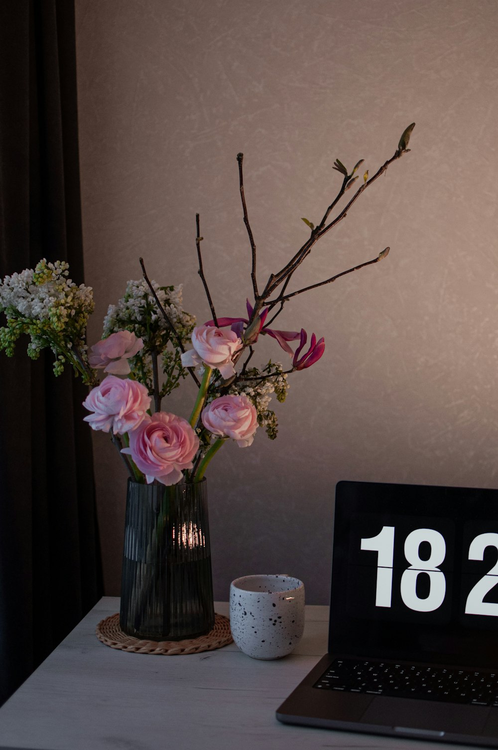 a desk with a laptop and flowers in a vase