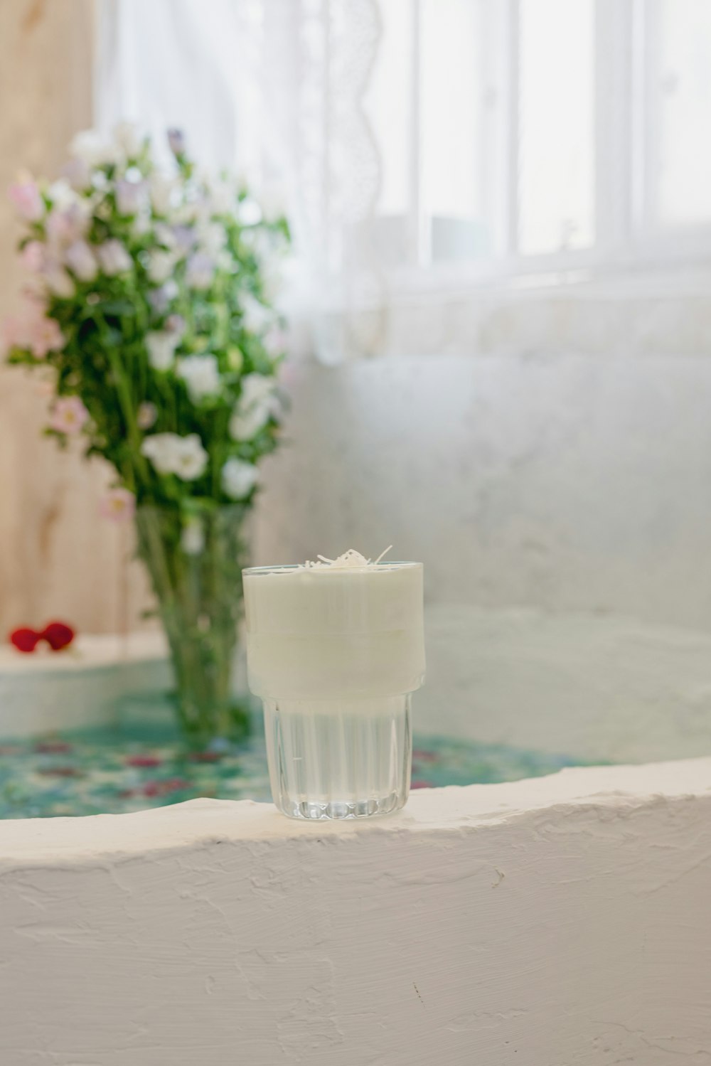 a glass of water sitting on a ledge next to a vase of flowers