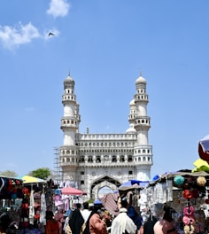 a crowd of people walking around a market under a blue sky