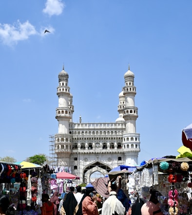 a crowd of people walking around a market under a blue sky