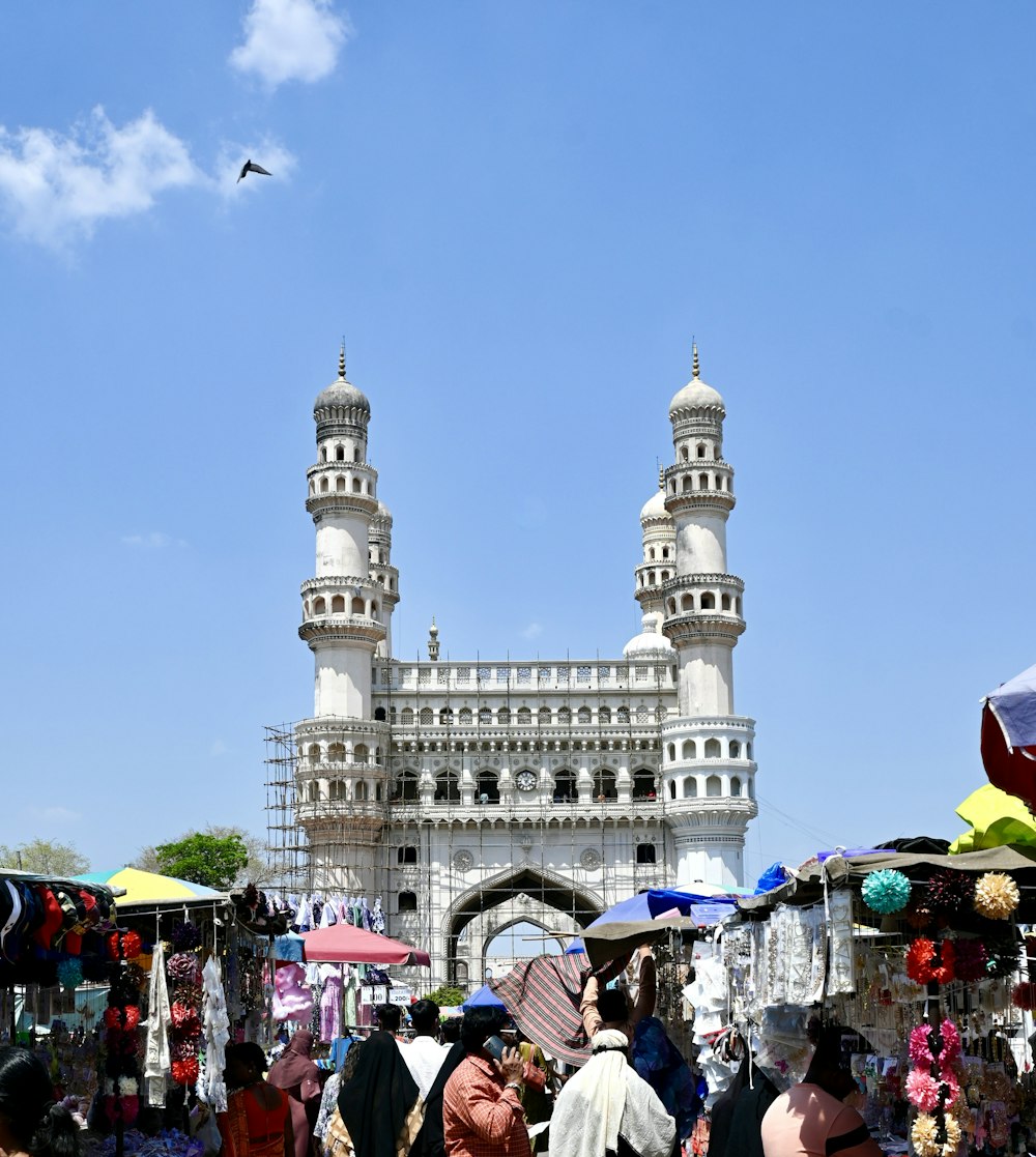 a crowd of people walking around a market under a blue sky