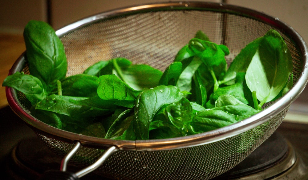 a colander filled with green leaves on top of a stove