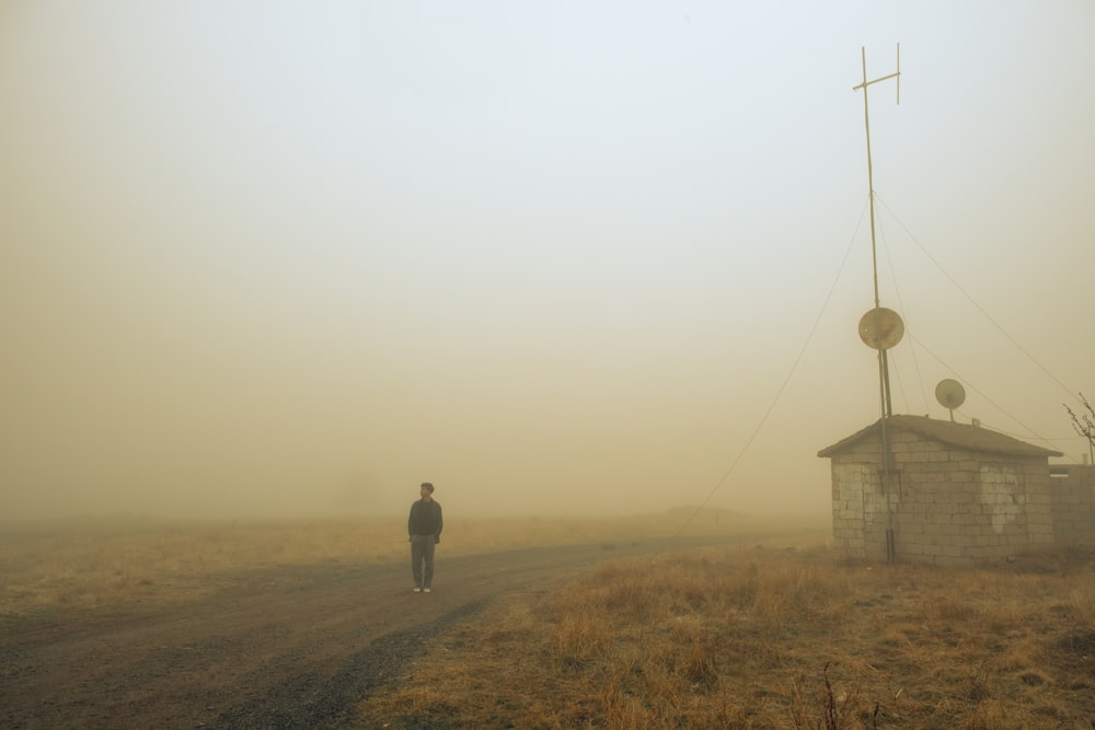 a man walking down a dirt road in the fog