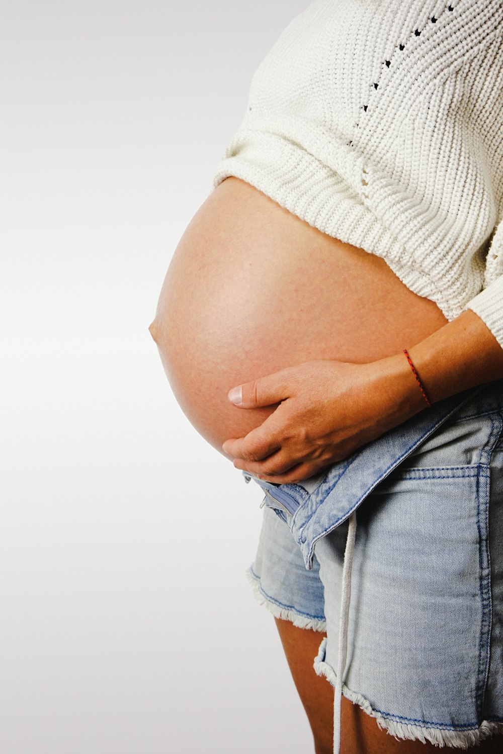 a pregnant woman in a white sweater and denim shorts