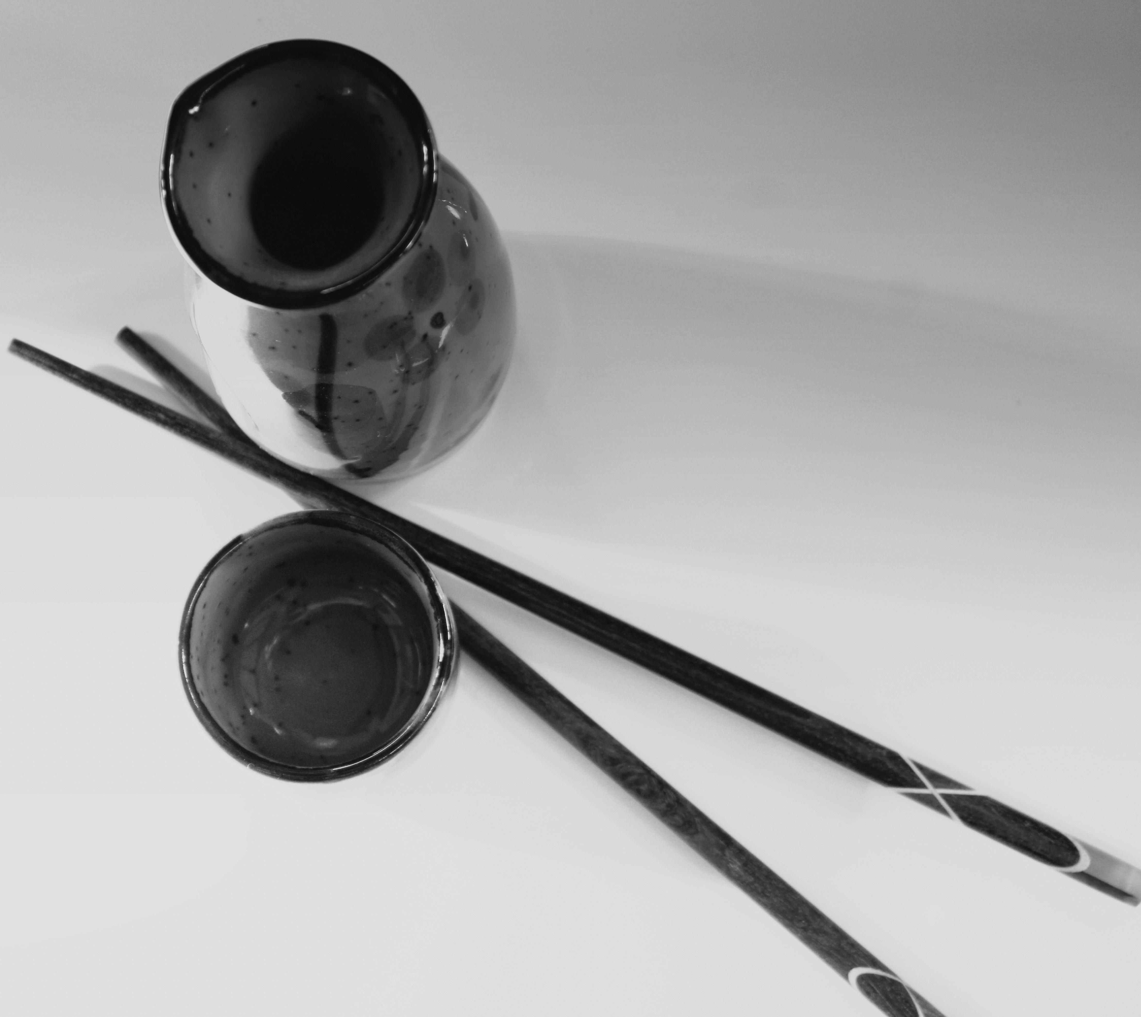 a black and white photo of a vase and two chopsticks
