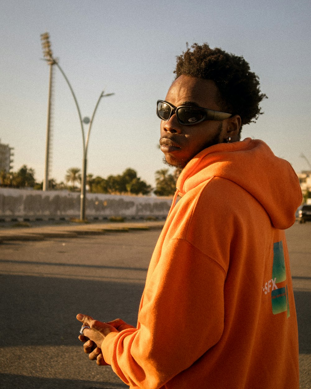 a man in an orange hoodie is standing on the street